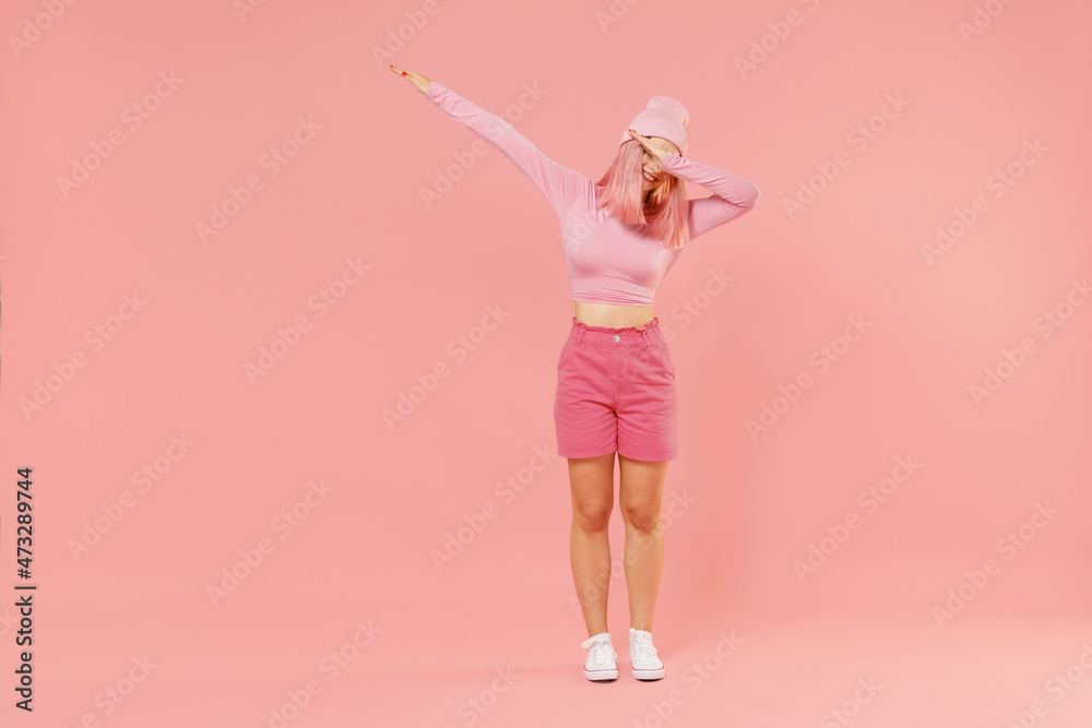 Full body young woman 20s with bright dyed rose hair in rosy top shirt hat doing dab hip hop dance hands move gesture isolated on plain light pastel pink background. People lifestyle fashion concept. Full body young woman 20s with bright dyed rose hair in rosy top shirt hat doing dab hip hop dance hands move gesture isolated on plain light pastel pink background. People lifestyle fashion concept.