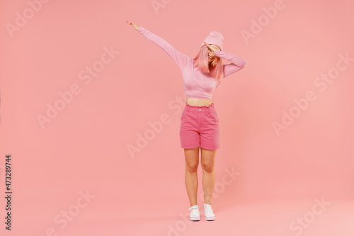 Full body young woman 20s with bright dyed rose hair in rosy top shirt hat doing dab hip hop dance hands move gesture isolated on plain light pastel pink background. People lifestyle fashion concept.