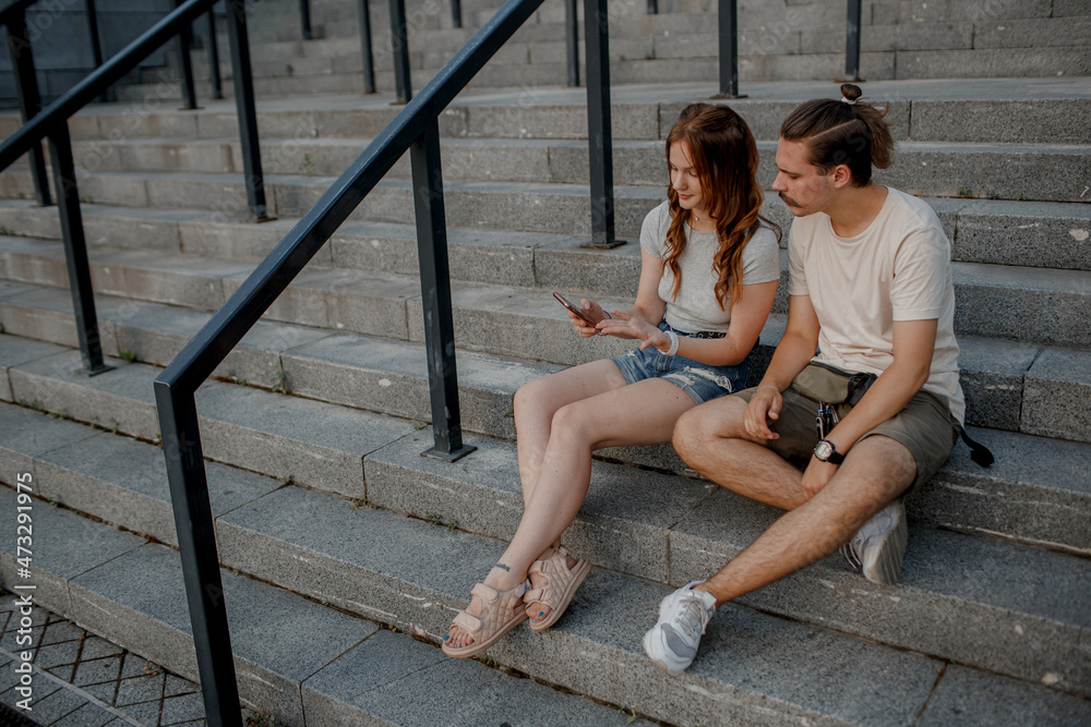 Charming couple is sitting on the stairs outside and watching in smartphone