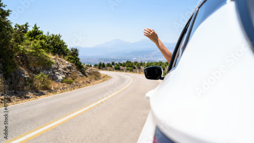 Woman sticking hand out from the open window driving a car. Trip on the serpentine road in the mountains. Summer vacation. Freedom concept. copy space