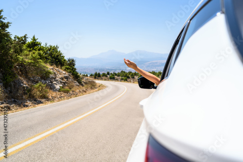 Woman sticking hand out from the open window driving a car. Trip on the serpentine road in the mountains. Summer vacation. Freedom concept. copy space