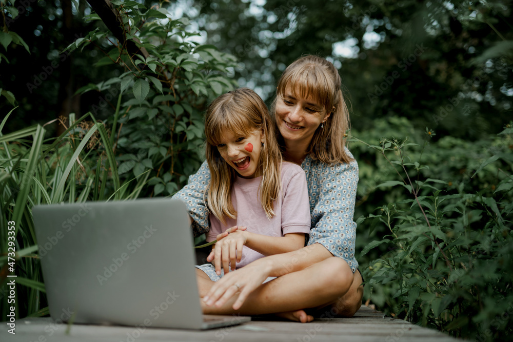 Mother with child are playing on laptop in the garden Mother with child are playing on laptop in the garden