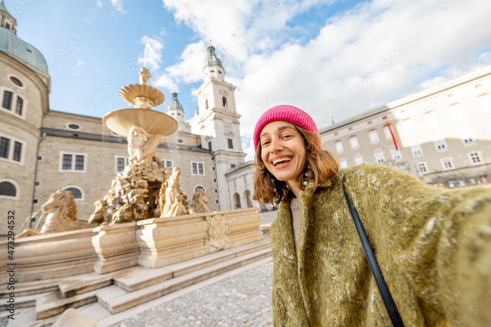 Fototapeta premium Woman visiting old town in Salzburg, standing on Residence square with famous fountain and cathedral on background. Traveler visiting Austria landmarks