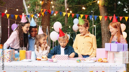 Canvas Print Portrait of happy child boy having fun to opening present at the table with his friends