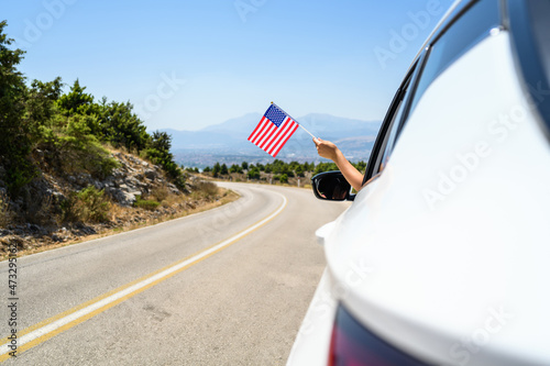 Woman holding USA flag from the open car window driving along the serpentine road in the mountains. Concept