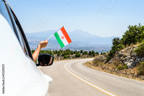 Woman holding Iran flag from the open car window driving along the serpentine road in the mountains. Concept