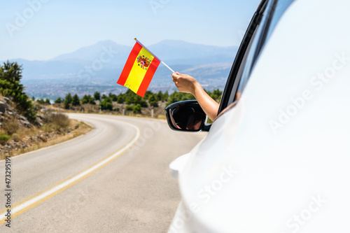 Woman holding Spain flag from the open car window driving along the serpentine road in the mountains. Concept