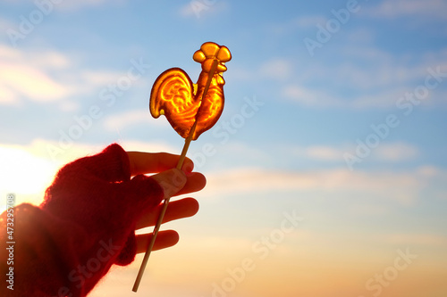 Foto Sweet lollipop cockerel on stick in the hand on sky background