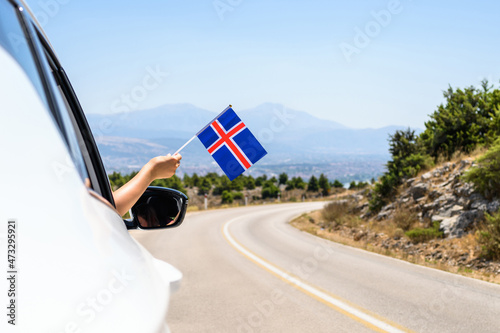 Woman holding Iceland flag from the open car window driving along the serpentine road in the mountains. Concept