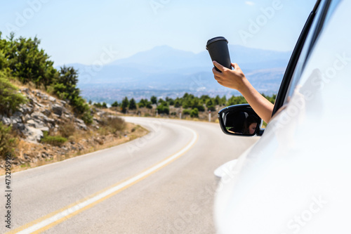 Woman driving a car holding paper cup of coffee from the open window. Trip on the serpentine road in the mountains. Summer vacation © flowertiare