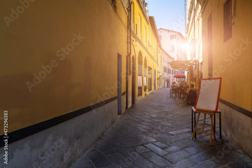 Lucca, Tuscany, Italy. August 2020. In an alley in the historic center, the tables of a restaurant with seated customers. Street paved with stones, the colorful facades of the houses frame it.