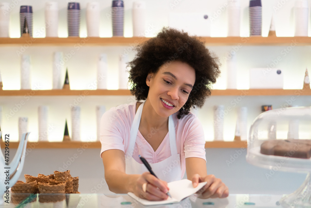 A beautiful mixed-race female worker in an ice cream parlor writes down an order. A beautiful mixed-race female worker in an ice cream parlor writes down an order.