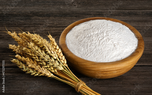 Bowl with flour and spikelets of wheat on wooden background.