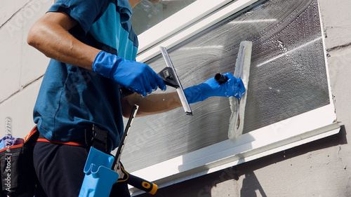 Male professional cleaning service worker in overalls cleans the windows and shop windows of a store with special equipment photo