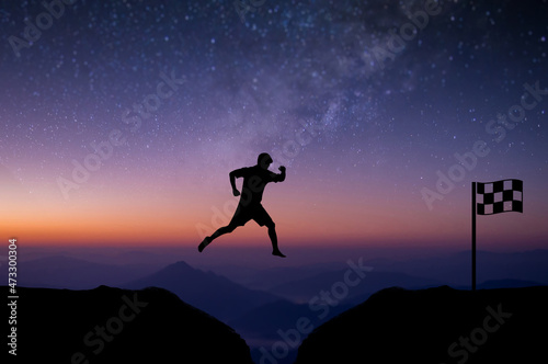 Young man jumping over precipice between two mountains cross the finish line with beautiful night sky, star and Milky Way over the sky. showing determination, freedom, risk, challenge, success.