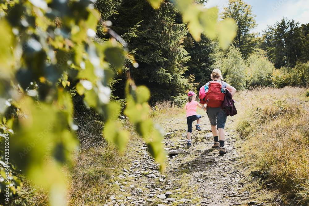 Obraz premium Family trip in mountains. Mother with little girl walking on path in forest, actively spending summer time together. Enjoying the outdoors in the summer trip vacation