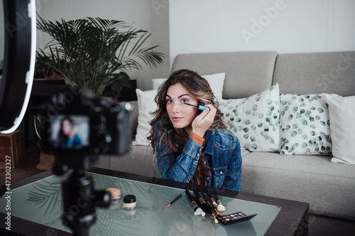 Vlogger applying mascara and filming through home video camera at table photo