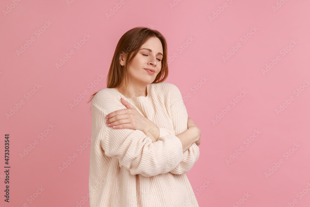 I love myself. Portrait of woman hugging herself and smiling, feeling comfortable and fulfilled, narcissistic egoistic person, wearing white sweater. Indoor studio shot isolated on pink background. I love myself. Portrait of woman hugging herself and smiling, feeling comfortable and fulfilled, narcissistic egoistic person, wearing white sweater. Indoor studio shot isolated on pink background.