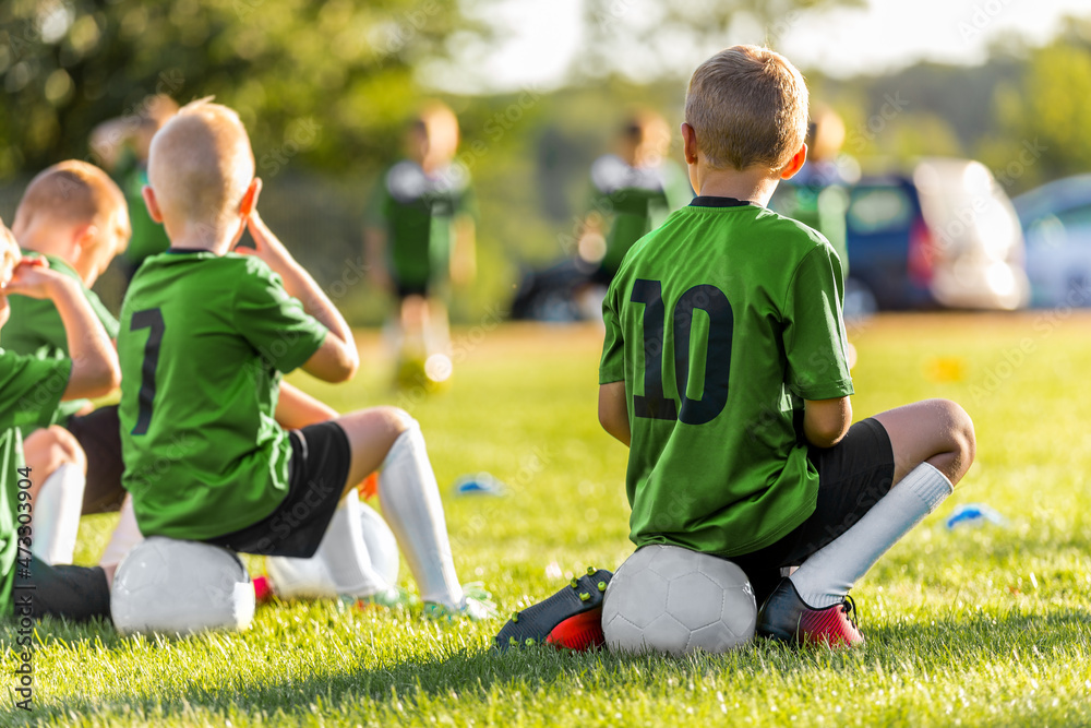 Group of Young Boys Kicking Sports Soccer Game on Grass Pitch. Boys Sitting on Soccer Balls Waiting to Play the Game. Friends in Sports Team. School Boys on Sideline. Kids in Green-Sports Shirts Group of Young Boys Kicking Sports Soccer Game on Grass Pitch. Boys Sitting on Soccer Balls Waiting to Play the Game. Friends in Sports Team. School Boys on Sideline. Kids in Green-Sports Shirts