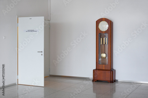 A large modern grandfather clock with weights and pendulum in a white empty room. photo