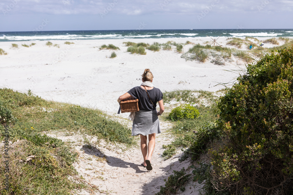 Adult woman carrying picnic basket on Grotto Beach, Hermanus, Western Cape, South Africa. Adult woman carrying picnic basket on Grotto Beach, Hermanus, Western Cape, South Africa.