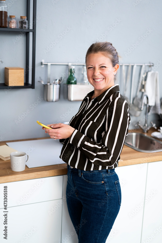 Happy woman holding mobile phone at kitchen counter Happy woman holding mobile phone at kitchen counter