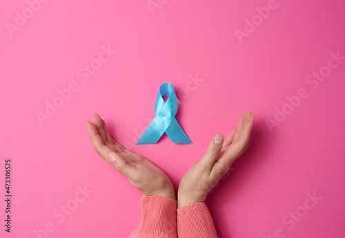 woman hands holding light blue ribbon awareness on a pink background. Men's health and prostate cancer awareness campaign concept.