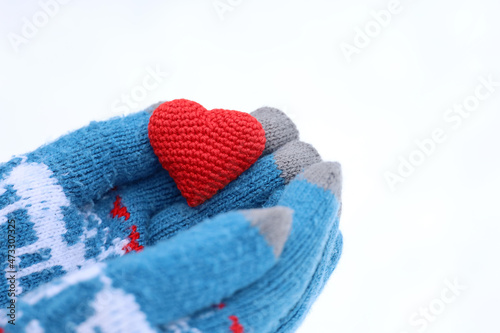 Love heart in palms of hands in warm knitted gloves against the white snow. Concept of Valentine's day, Christmas celebration or charity