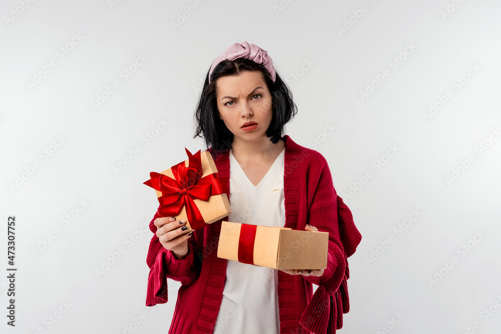 Portrait of a discouraged young woman opening a gift box decoration red ribbon, isolated over white background Portrait of a discouraged young woman opening a gift box decoration red ribbon, isolated over white background