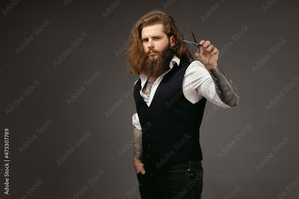 man with a beard in a vest holds scissors in his hands