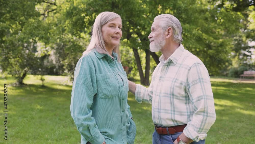 Full length view of the pretty mature husband and wife are standing at the grass and embracing in park. They are smiling Full length view of the pretty mature husband and wife are standing at the grass and embracing in park. They are smiling