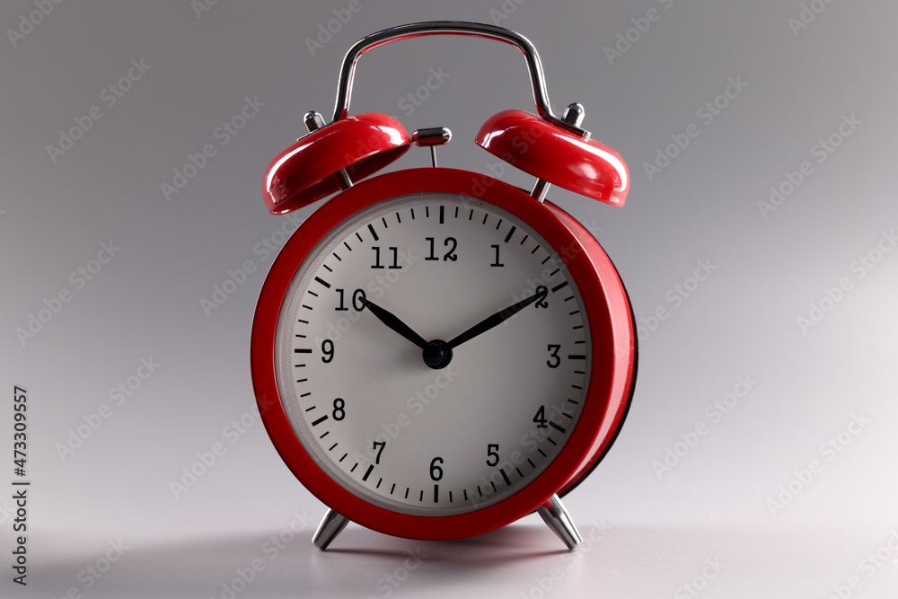 Red classic alarm clock standing on gray background closeup Red classic alarm clock standing on gray background closeup