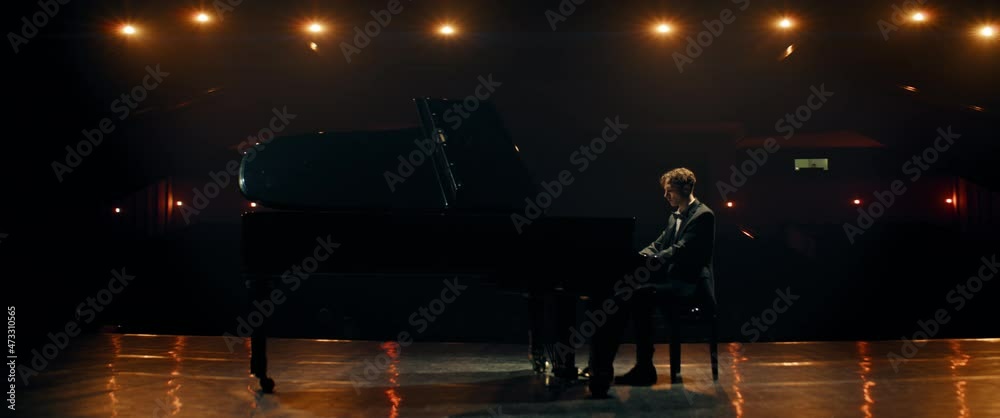 WIDE Young 20s aspiring musician playing grand piano on a stage of a huge concert hall. Shot with 2x anamorphic lens