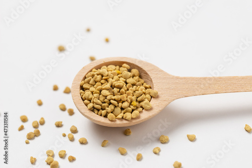 Horizontal macro photo of dietary supplement bee pollen in a wooden spoon on white. Top view