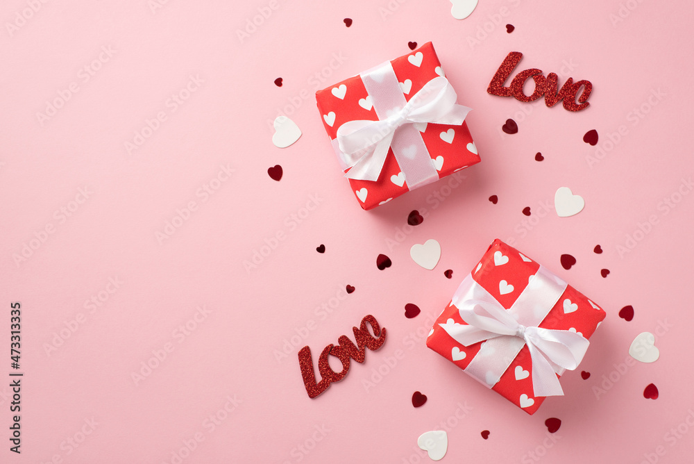 Top view photo of valentine's day decorations two gift boxes in red wrapping paper with pattern of hearts inscriptions love paper hearts and confetti on isolated pastel pink background with copyspace