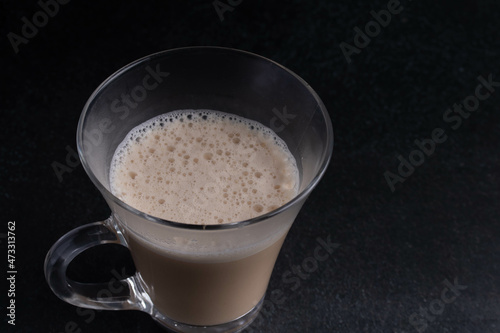 Latte iced coffee in a clear glass on a black background.