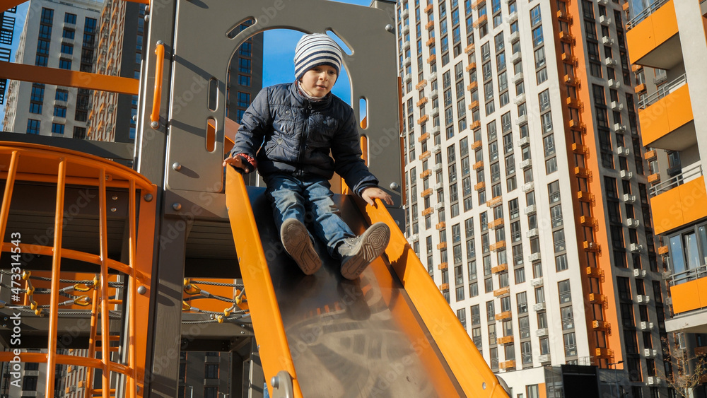 Happy smiling boy riding down slide on modern children playground Happy smiling boy riding down slide on modern children playground