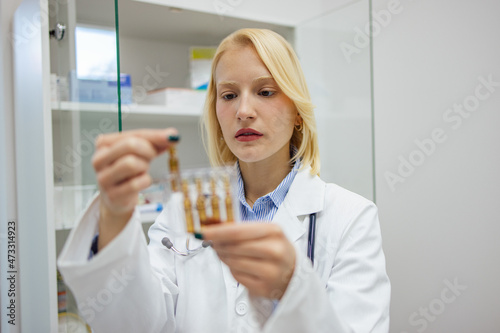 Blonde caucasian female doctor  going to a lab and examining the vial.