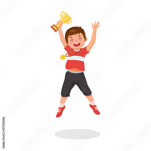 little boy jumping holding a gold cup trophy celebrating winning competition first prize