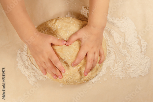 Children's hands lie in the shape of a heart on a curd dough on a background of baking paper sprinkled with white flour