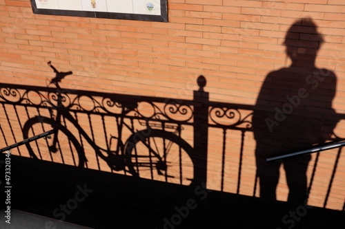 Ombres sur un mur ocre. Vélo et homme appuyés à une balustrade dans la rue.