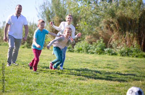 Father with mother with two children enjoy playing soccer on lawn in summer park