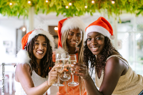 Happy smiling African American girls celebrating Christmas (or new year) and cheering with champagne. Winter holidays and multiracial group concept. Focus on glasses