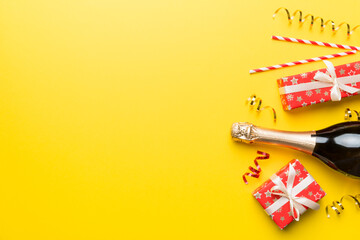 Bottle of champagne with colored glitter, confetti and gift box space for text on colorfull background, top view. Hilarious, christmas and birthday celebration