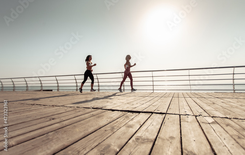 Two athletic women friends running along the embankment in the early morning