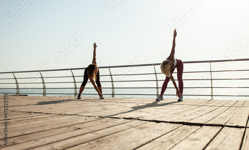 Two athletic women warming up doing exercises early morning on the beach