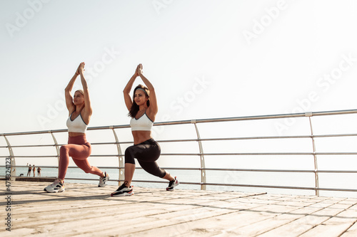 Two athletic women doing lunges together on the beach, working out their leg muscles. Healthy lifestyle