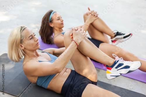 Two beautiful athletic women practicing leg stretching together while lying on mat