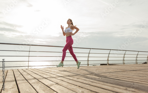 Young woman in sportswear jogging along the beach in the early morning. Healthy lifestyle, cardio workout