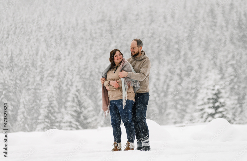 Walk in winter. Embracing couple enjoying snowfall. Man and woman having fun in the frosty forest. Romantic date in winter time.Christmas mood of a young family. Love and leisure concept